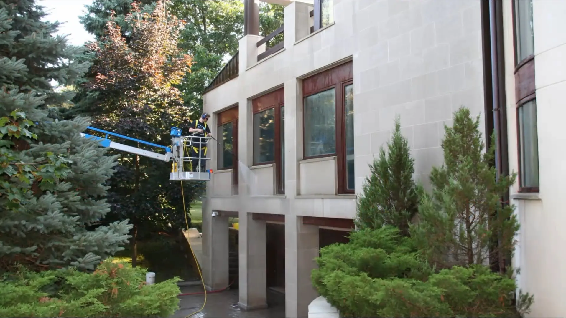 A Revive technician pressure washing a building exterior from a lift